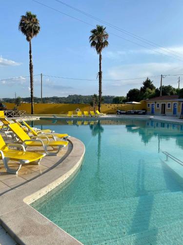 a large swimming pool with yellow chairs and palm trees at Charm Azenha DÓbidos Farm in Olho Marinho