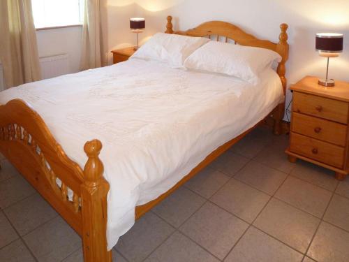 Schlafzimmer mit einem Holzbett mit weißer Bettwäsche und Kissen in der Unterkunft Old Barn Holiday Cottage by Trident Holiday Homes in Skibbereen