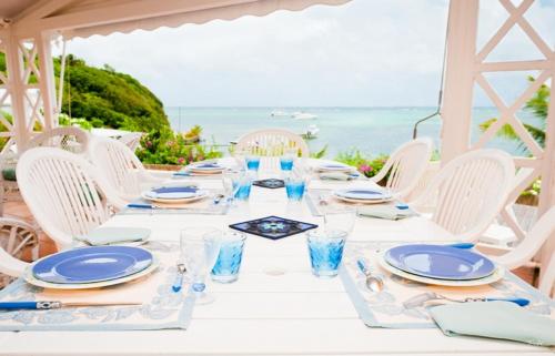 una mesa blanca con platos y vasos azules y el océano en BRIN d AMOUR COTE ATLANTIQUE voir site vacances en martinique, en La Trinité