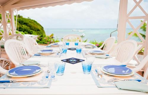 a white table with blue plates and glasses and the ocean at BRIN d AMOUR COTE ATLANTIQUE voir site vacances en martinique in La Trinité