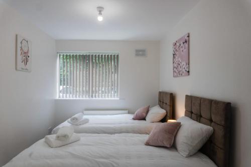 two beds in a white bedroom with a window at Gorgeous ground floor apartment + free parking in Manchester