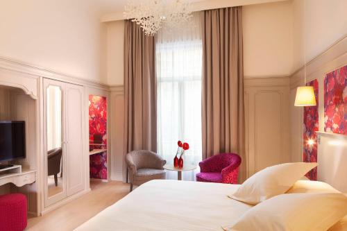 a bedroom with a bed and two chairs and a television at Hôtel & SPA Oceania L'Univers Tours in Tours