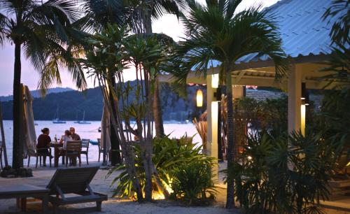 people sitting at a table under palm trees on the beach at The Cove in Panwa Beach