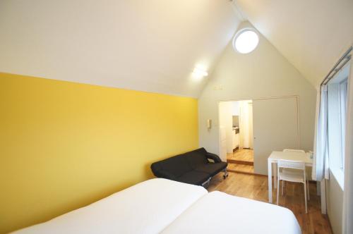 a bedroom with a yellow wall and a bed and a chair at Plusone Nishikoen in Fukuoka