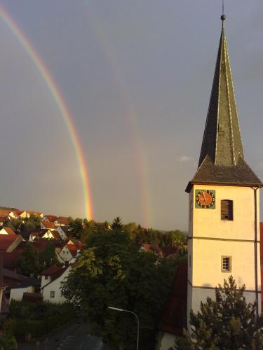 Un arcobaleno sopra una chiesa con una torre dell'orologio di Pension Rose a Bretzfeld