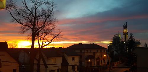 a sunset over a city with a clock tower at Ave Łagiewniki in Kraków