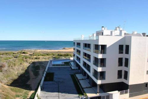 ein weißes Gebäude mit dem Ozean im Hintergrund in der Unterkunft Pinada Beach IV new & comfort. apartment, 1st line to the beach, sunterrace+pool in La Mata