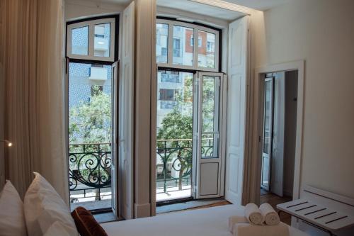 a bedroom with three windows and a bed and a balcony at Le Premier Lisbon Suites in Lisbon