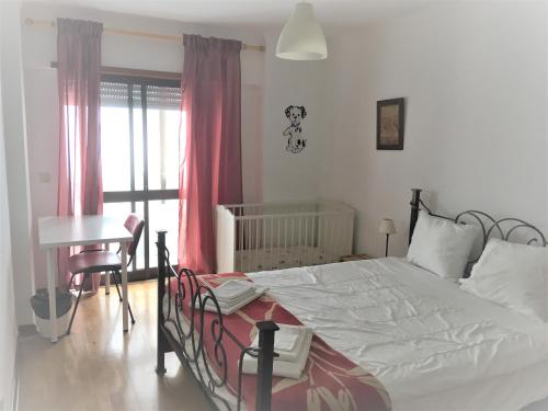 a bedroom with a bed and a table and a crib at Apartamento Familiar Lisboa Taguspark in São Marcos