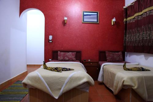 two beds in a room with a red wall at Western Desert Hotel & Safari in Bawiti