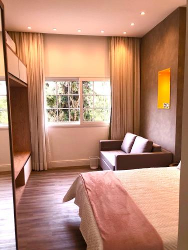 a bedroom with a bed and a couch and window at Lindo Loft Itaipava RJ in Itaipava