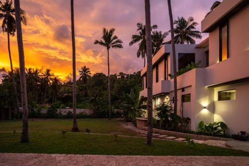 DekeにあるAlamayah Boutique Retreat Hotelの夕日の前にヤシの木が茂る建物