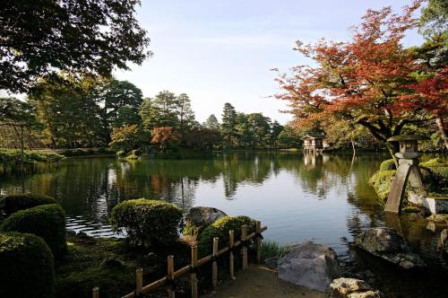a pond in a garden with a bridge and trees at Kenroku House in Kanazawa