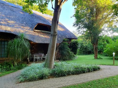 a thatch roofed house with a table and chairs at Shingalana Guest Lodge in Hazyview