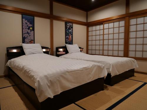 dwa łóżka w pokoju z oknami w obiekcie SAKURA Aburaya w mieście Takayama