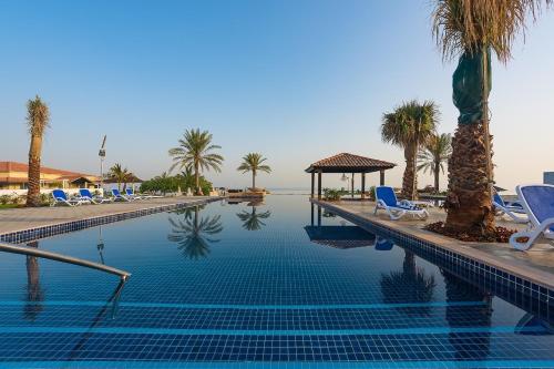 einen Pool mit Stühlen und Palmen in der Unterkunft Barracuda Resort in Umm al-Qaiwain