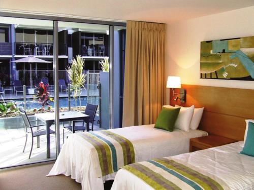 a hotel room with two beds and a table and a balcony at Ramada by Wyndham Hervey Bay in Hervey Bay