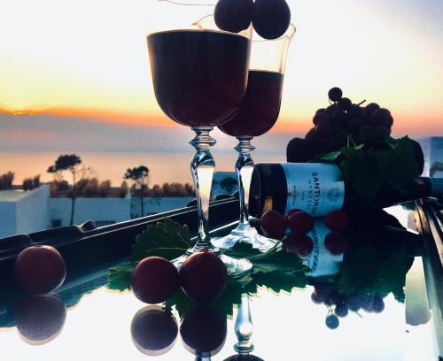 two glasses of wine sitting on a table with grapes at Santolia Art Suites in Oia