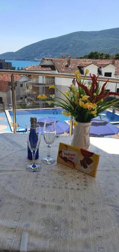 a table with two wine glasses and a vase with flowers at Apartmani Niksic in Herceg-Novi