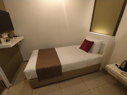 a small bedroom with a bed with a red pillow at Crescendo Boutique Hotel in Nusajaya
