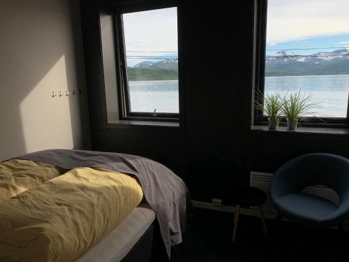a bedroom with a bed and a chair and two windows at BEDEHUSET Basecamp Senja in Skaland