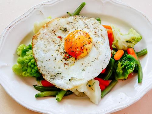 a white plate with a fried egg on top of vegetables at Oberża Złota Gęś in Siewierz