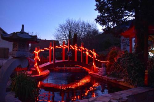 un pont sur un étang avec des lumières rouges dans l'établissement Gîte Au printemps Japonais, petit train de la Mure, parc des Ecrins, à Pierre-Châtel