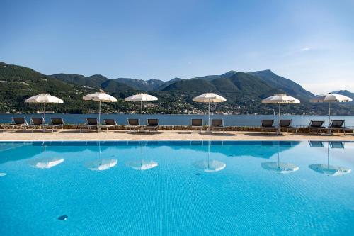 a swimming pool with umbrellas and chairs and the water at Park Hotel Casimiro in San Felice del Benaco