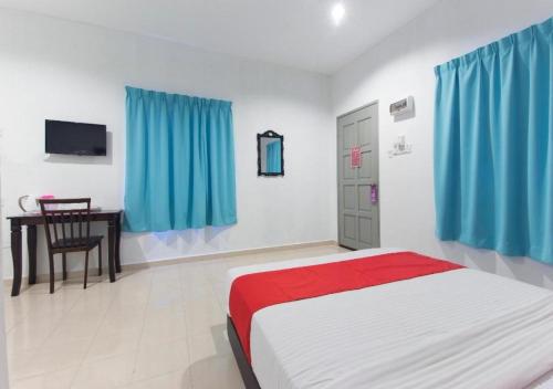 a bedroom with a bed and a desk and blue curtains at Alpha Motel in Pantai Cenang
