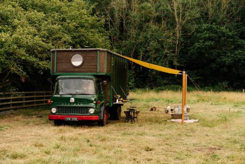 Ein grüner Truck parkt auf einem Feld mit einem Haus darauf. in der Unterkunft Abbeyfield Horsebox Glamping in Morpeth