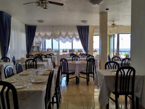 une salle à manger avec des tables blanches, des chaises et des fenêtres dans l'établissement Hotel Morri, à Bellaria-Igea Marina