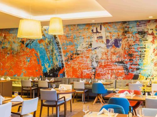 a restaurant with tables and chairs and a large mural at Novotel Porto Alegre Airport in Porto Alegre