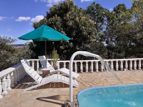 uma piscina com uma mesa e um guarda-sol e cadeiras em Pousada Travessias em Tiradentes