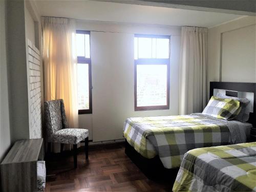 um quarto com 2 camas, uma cadeira e 2 janelas em Royalty Inn em Lima