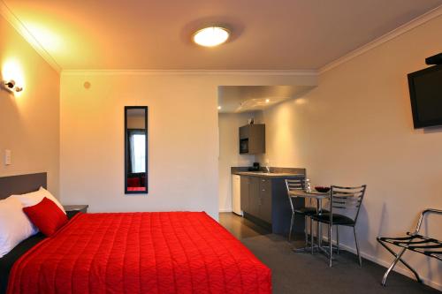 a hotel room with a red bed and a kitchen at Oamaru Motor Lodge in Oamaru