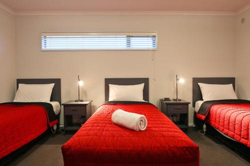 Oamaru Motor Lodge في أومارو: غرفة نوم بسريرين مع شراشف حمراء ومخدة بيضاء