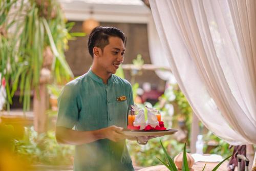a man holding a plate with a piece of cake at Cambana d'Angkor Suites in Siem Reap