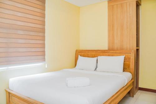 a bedroom with a white bed with a wooden headboard at Tidy 2BR Apartment at Silkwood Residences near BINUS By Travelio in Tangerang