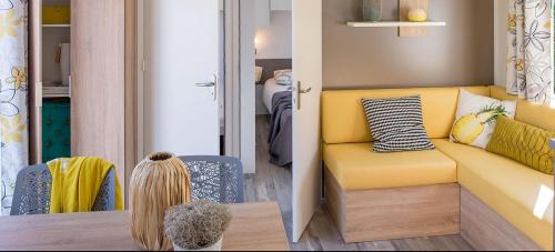 a living room with a yellow couch and a table at Camping la Haie Penée **** in Saint-Quentin-en-Tourmont