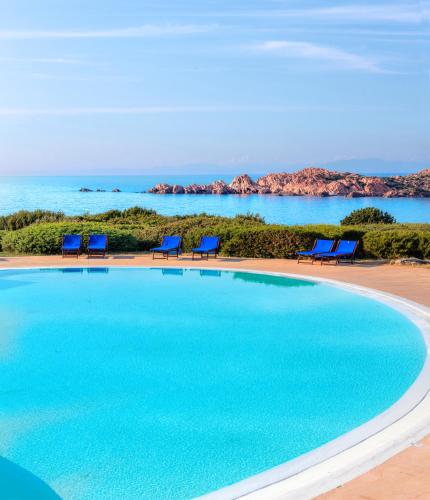 a swimming pool with chairs and the ocean in the background at Hotel Relax Torreruja Thalasso & Spa in Isola Rossa