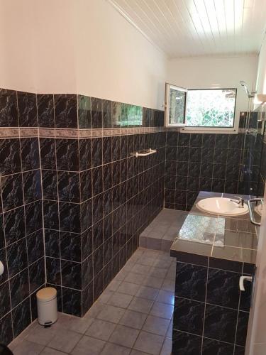 a black tiled bathroom with a sink and a mirror at Hotel La Chaumiere in Matoury