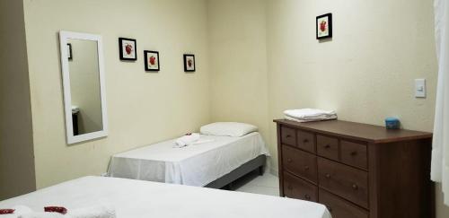 a bedroom with two beds and a dresser and a mirror at Condomínio Village, Casa Cecília in Maragogi