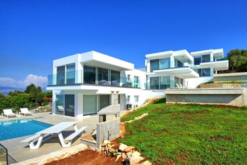 a large white house with a swimming pool and chairs at Villa Nafsika by PosarelliVillas in Perítheia