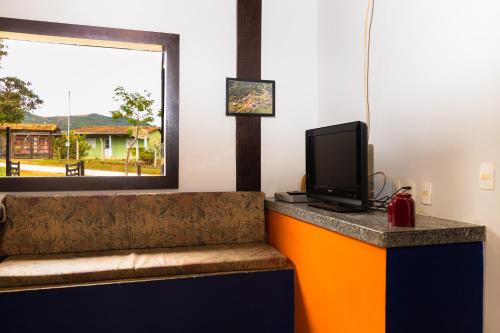 a room with a couch with a tv and a window at Estâncias da Serra dos Alves in Itabira
