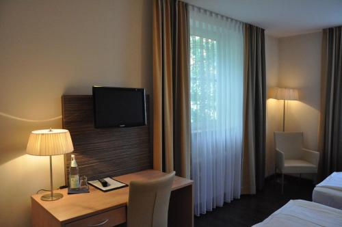 ein Hotelzimmer mit einem Schreibtisch und einem TV am Fenster in der Unterkunft Gästehaus der Katholischen Akademie in Regensburg