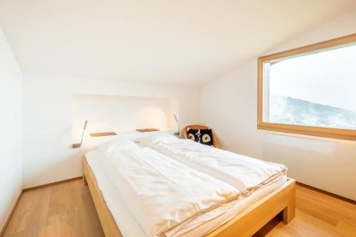 a white bedroom with a bed and a window at LAAX Homes - Casa Fau in Laax