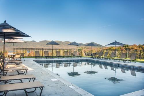 a swimming pool with chairs and umbrellas and tables at The Mountain Top Inn & Resort in Chittenden