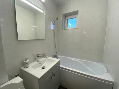a white bathroom with a sink and a tub and a mirror at Best Apartment City Hall in Suceava
