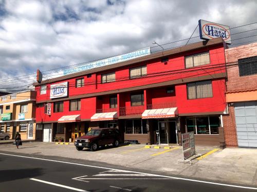 a red building with a truck parked in front of it at Hostal Mitad del Mundo in Cayambe