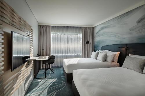 a hotel room with two beds and a desk at Novotel Tainui Hamilton in Hamilton